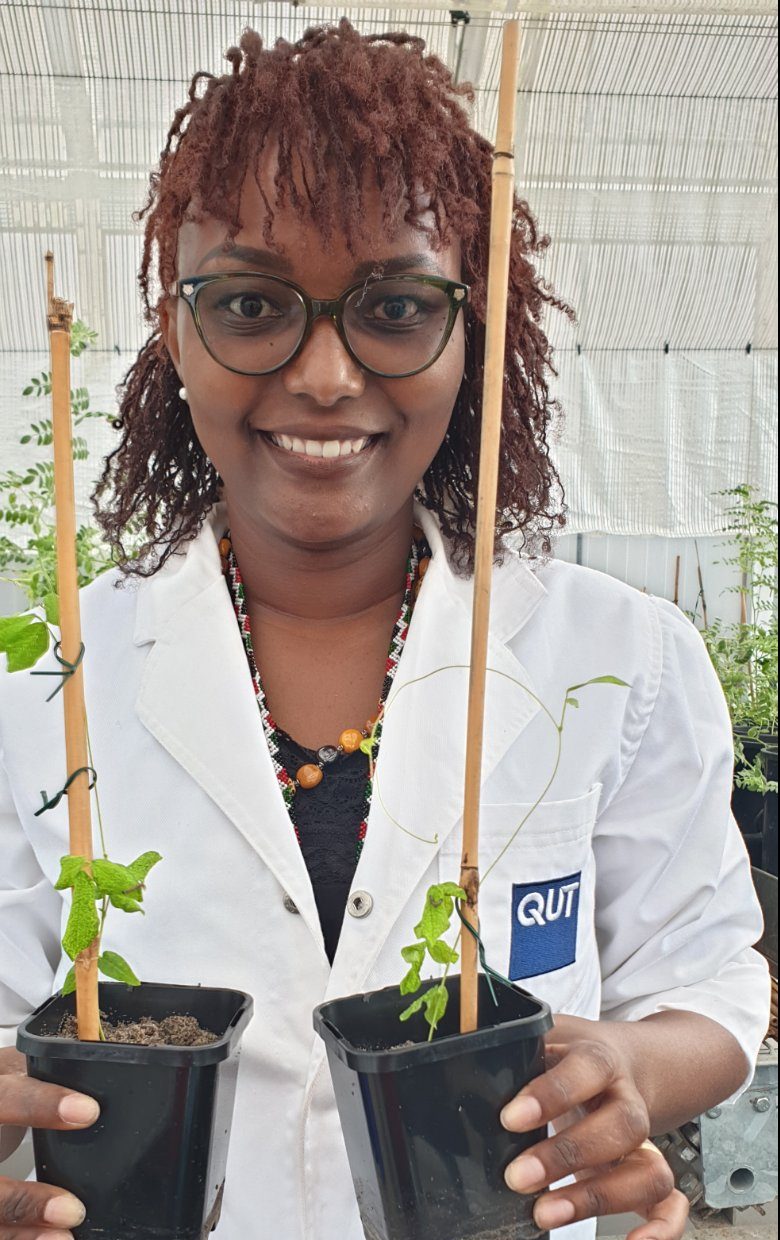 Abigail holding plants wearing a QUT lab coat 