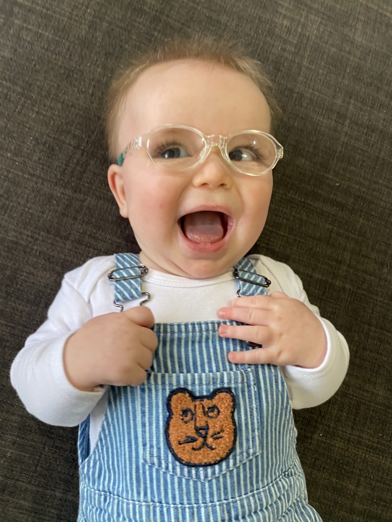 Max smiling wearing glasses in teddy dungarees