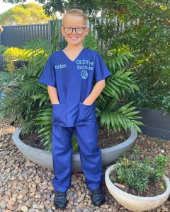 Photo of Korbin wearing hand made blue scrubs facing the camera and smiling