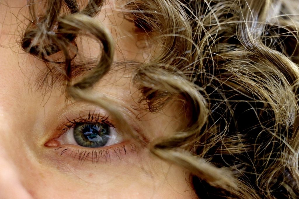 Picture of person's left eye looking at camera with curly brown hair partially covering this face