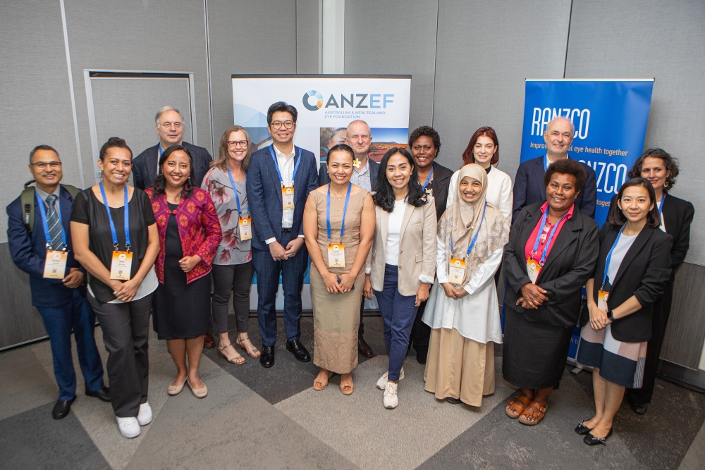 A large group of men and women, most of whom appear to be of Asian or South Pacific heritage, stand in front of banners with branding for the Royal Australian and New Zealand College of Ophthalmology and Australia and New Zealand Eye Foundation