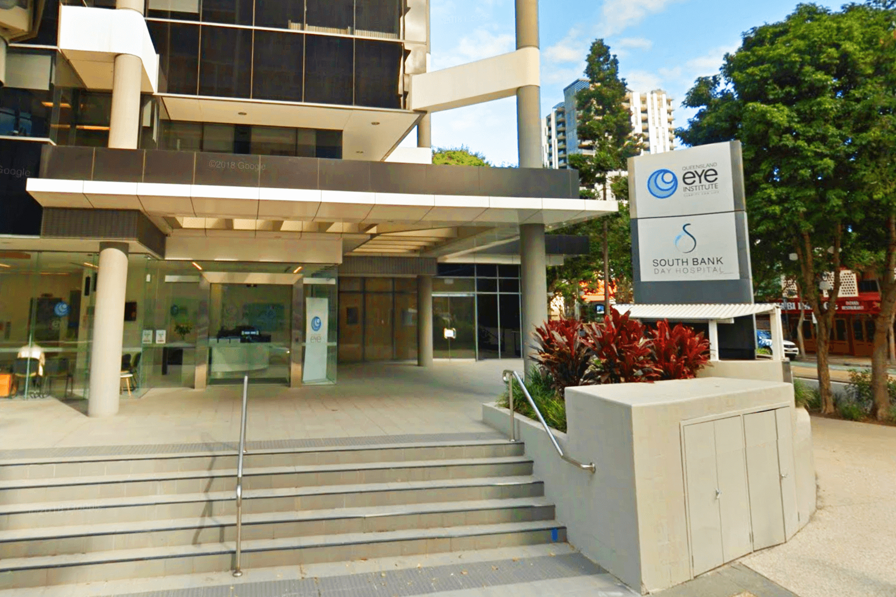 A tall building with large glass doors and concrete pillars with a sign at the front reading "Queensland Eye Institute and South Bank Day Hospital"