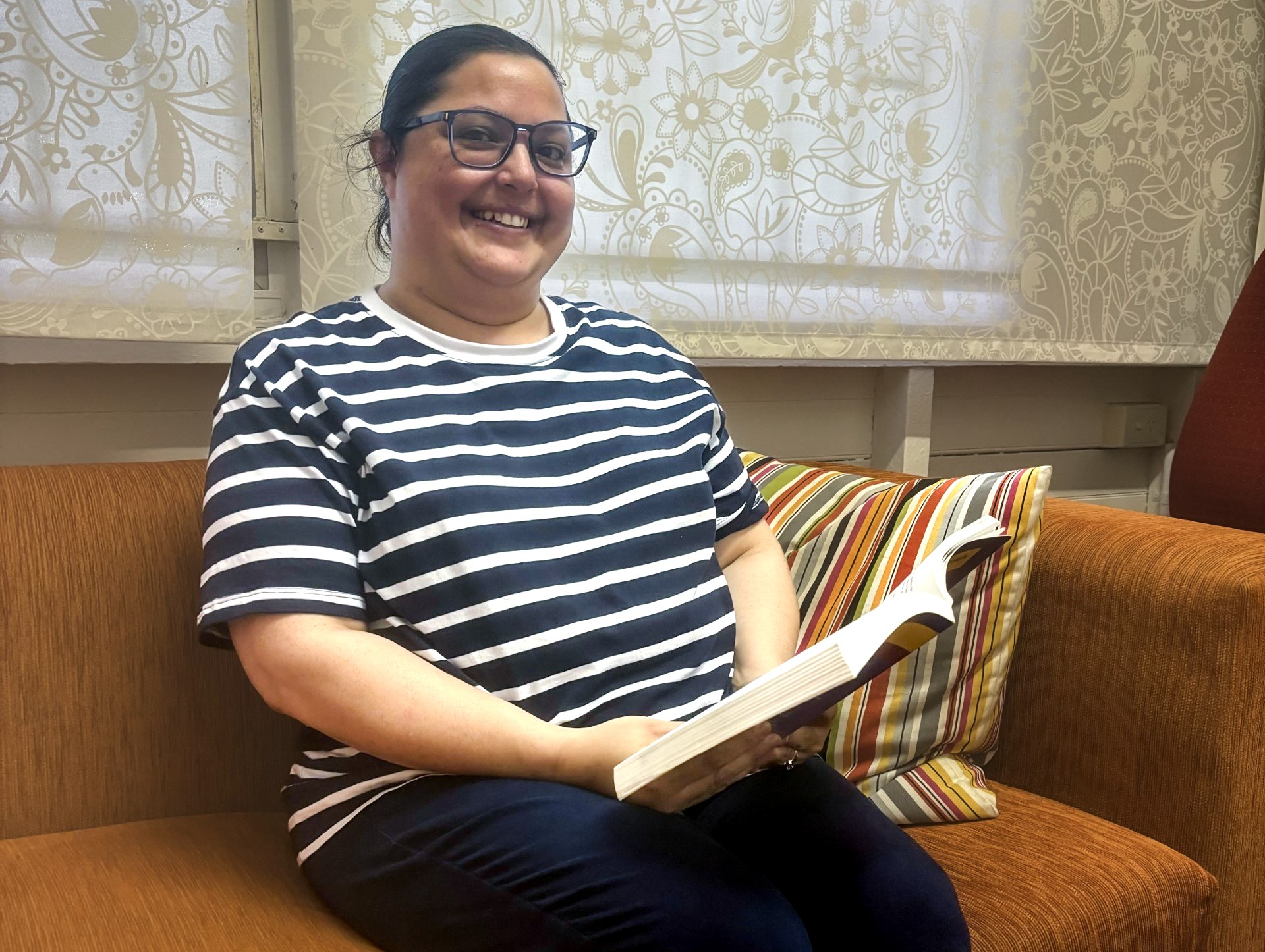 Sarah Oakleigh seated on sofa reading a book