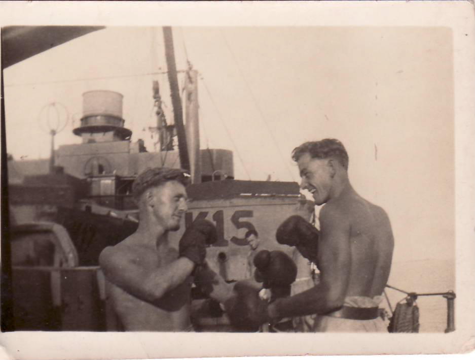 Old black and white photo of two sailors, shirtless, boxing on the deck of a large ship