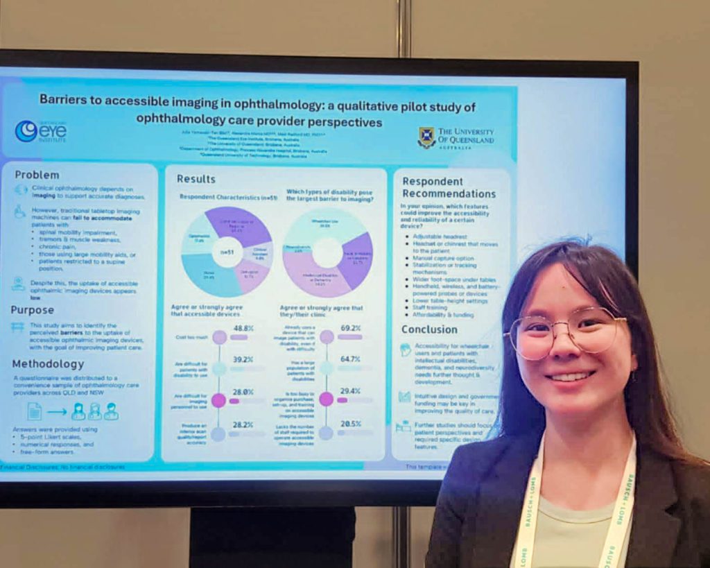 A young woman with long brown hair smiles at the camera. Behind her is a large digital screen with an image of a research poster.