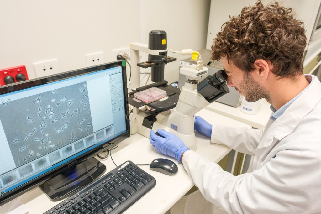 A young man with curly hair looks through a microscope. 